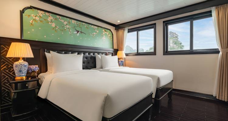 Bright twin-bed cabin on a Halong Bay cruise ship with tufted headboard and view of limestone karsts through the window.