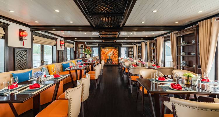 Full-length view of an elegant cruise dining room with orange seating and ornate ceiling panels.