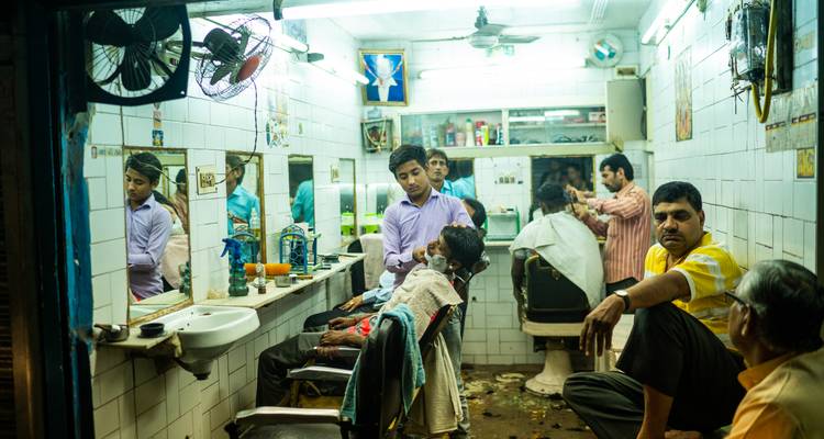 Barbería tradicional concurrida en Delhi con múltiples clientes y espejos