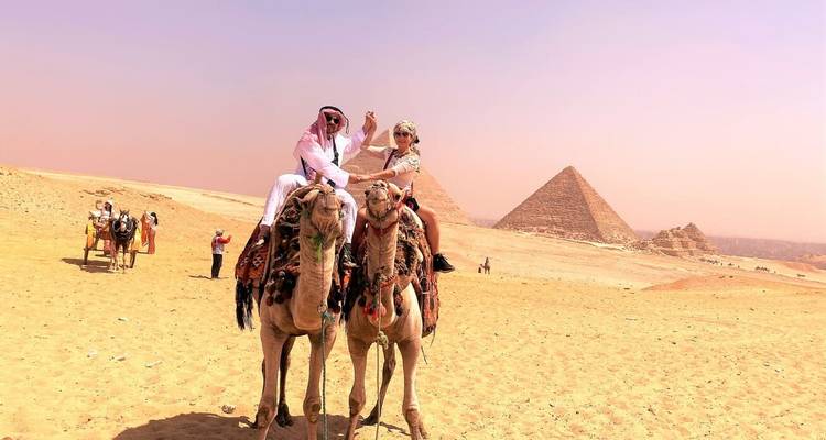 Zwei Menschen auf Kamelen in der Wüste mit Pyramiden.