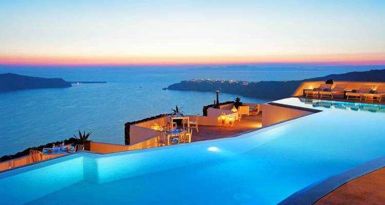 Piscina infinita con vista al mar al atardecer con configuración de cena romántica.