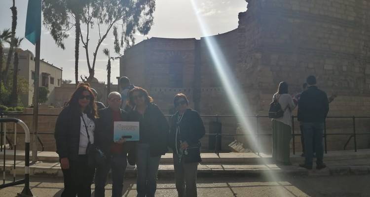 Een groep mensen buiten met een stenen structuur op de achtergrond.