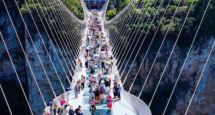 Un puente colgante de cristal abarrotado de gente atraviesa un profundo cañón entre acantilados boscosos en Zhangjiajie.