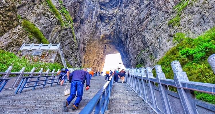 Los visitantes suben por empinadas escaleras de piedra hacia el arco natural de la Cueva Tianmen enmarcado por acantilados imponentes.