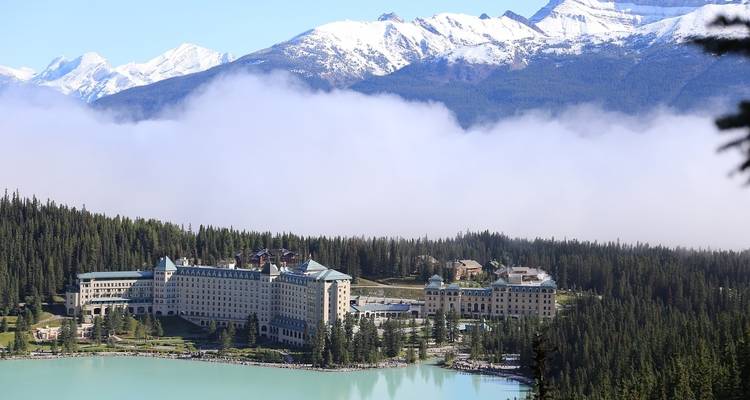 Gran hotel en medio de un bosque con montañas en la distancia.