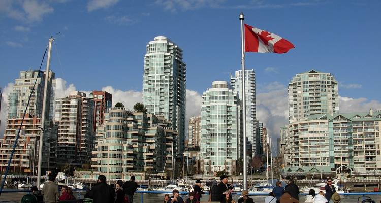 Les gens se rassemblent sur une promenade riveraine avec le drapeau canadien et des tours de condominiums modernes en arrière-plan.
