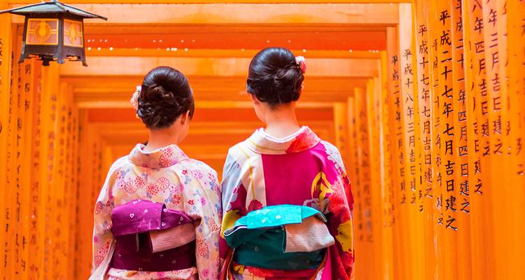 Deux femmes en kimonos colorés marchant à travers un tunnel de torii orange.