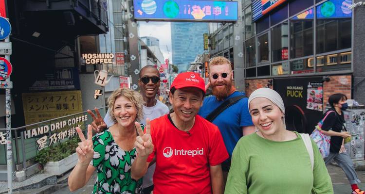 Viajeros sonrientes posando en una animada calle comercial japonesa llena de carteles coloridos y cafés.