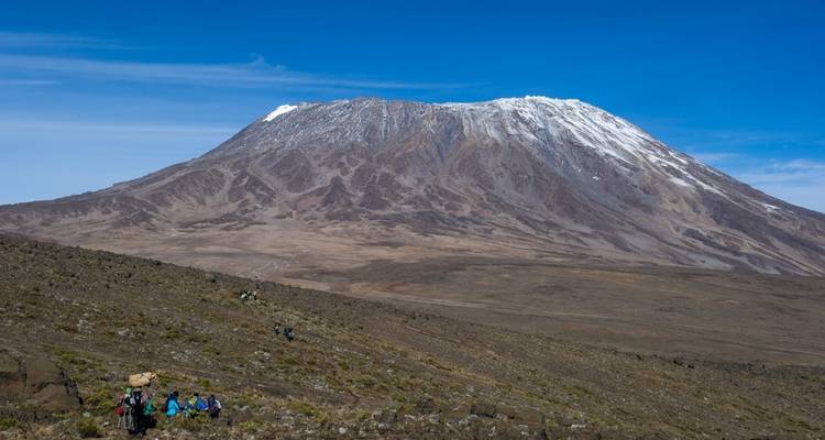 Der Kilimandscharo mit Wanderern auf einem Pfad im Vordergrund.