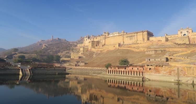 Amer Fort in Jaipur weerspiegeld in een waterpartij onder een heldere hemel.