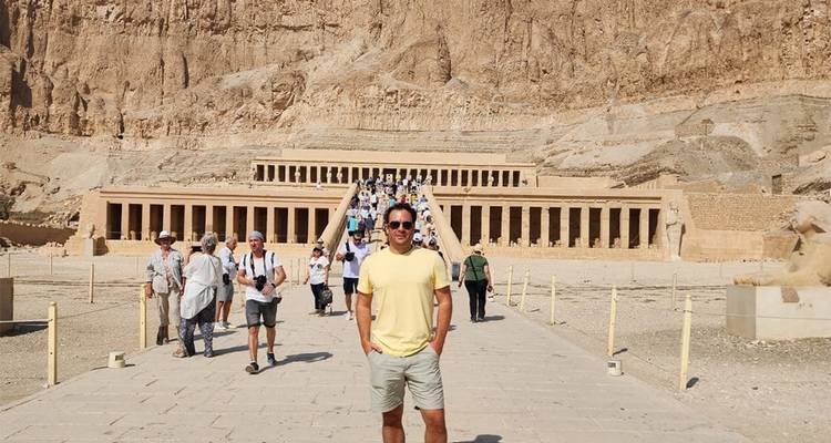 Personas caminando hacia un templo antiguo tallado en un acantilado.