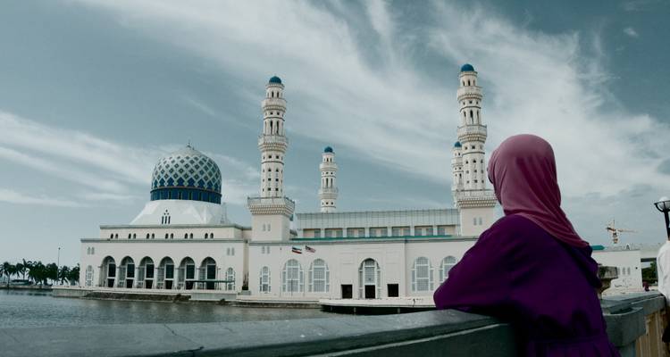 Une femme en hijab observant une belle mosquée au bord de l'eau.
