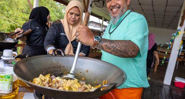 Les participants rient et mélangent les ingrédients dans un grand wok lors d'un cours de cuisine en plein air.
