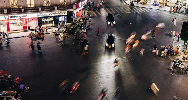 Un carrefour urbain animé la nuit avec des véhicules et des piétons en mouvement.