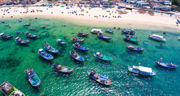 Vue aérienne de nombreux bateaux de pêche colorés dans une eau bleue claire.
