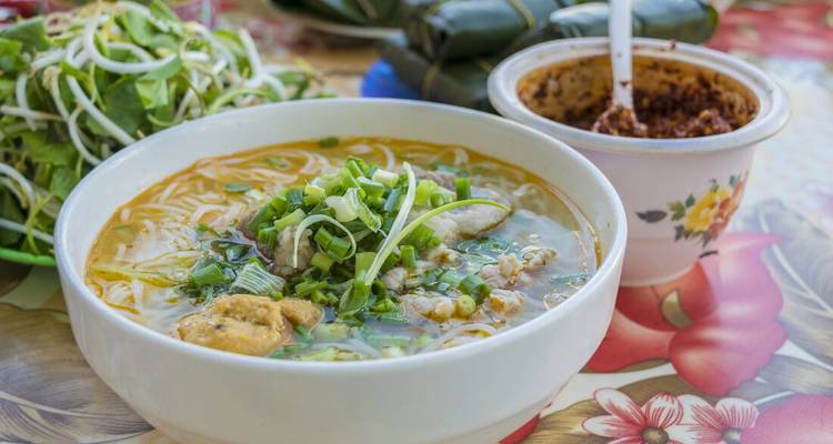 Bol de soupe de nouilles vietnamienne garnie d'herbes fraîches sur une table colorée.