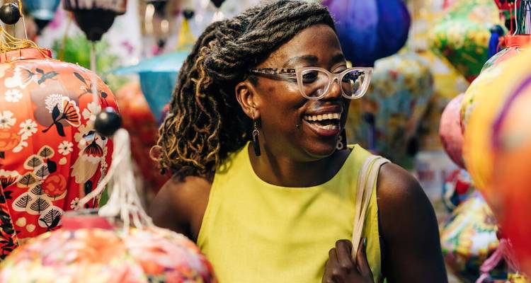 Femme souriante dans un marché vibrant entourée de lanternes en soie colorées.