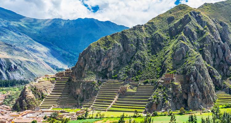 Terrasvormige Inca-ruïnes van Ollantaytambo met groene bergen en blauwe lucht op de achtergrond.