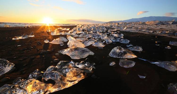 Black sand beach with illuminated ice chunks under a rising sun.