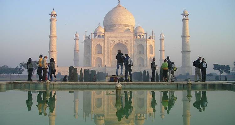De Taj Mahal met bezoekers en zijn spiegeling in een vijver.