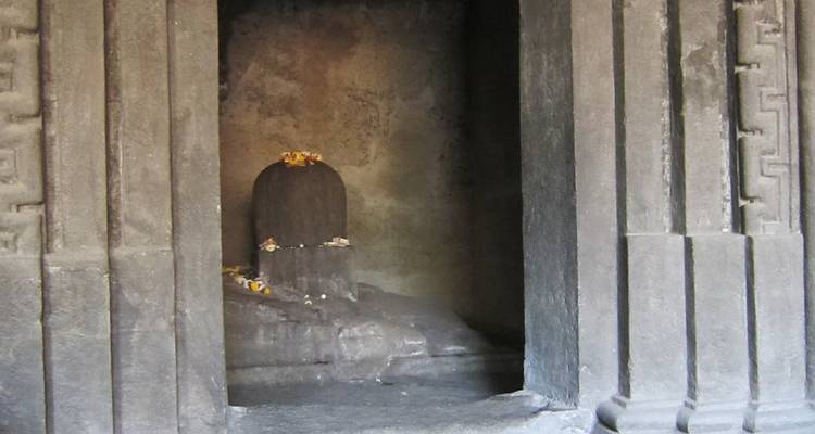 Linga idol surrounded by flowers in a stone alcove.
