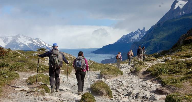 Senderismo en grupo por terreno rocoso con montañas nevadas a lo lejos.