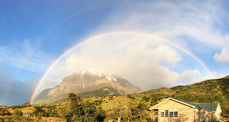 Un arcoíris sobre montañas y una pequeña casa de madera.