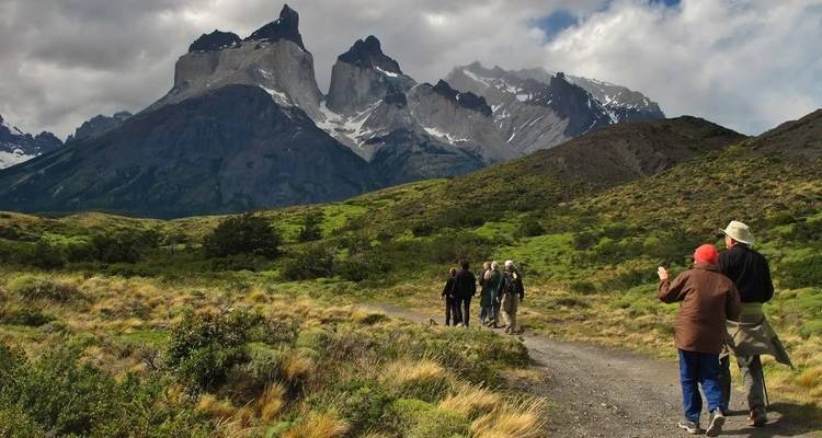 Grupo de personas haciendo senderismo con montañas dramáticas en el fondo.