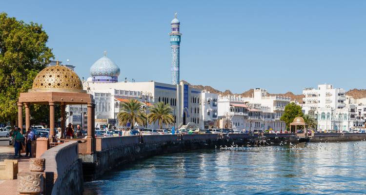 Zeepromenade van Muscat met een koepelmoskee en mensen die langs het rustige water slenteren.