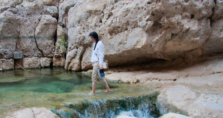 Une femme marchant dans de l'eau peu profonde dans un environnement rocheux.