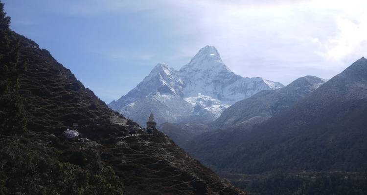 Le sommet à deux pointes d'Ama Dablam s'élève au-dessus d'une profonde vallée forestière dans une lumière claire.