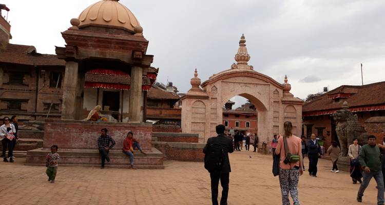 Historic courtyard with arched sandstone gateway and scattered visitors under cloudy skies