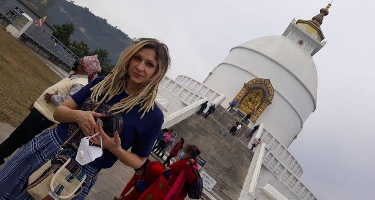 Visitor standing near the white World Peace Pagoda with golden doorway and sweeping stairs in Pokhara.