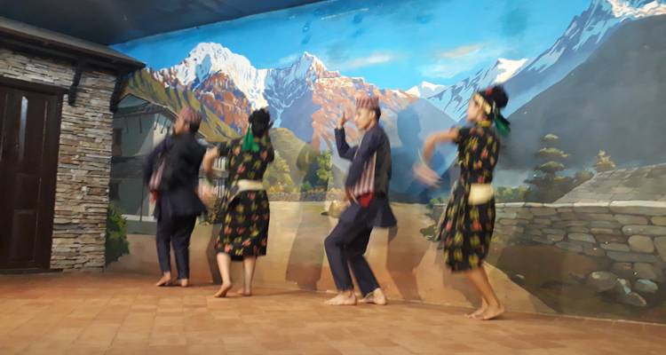 Traditional Nepali folk dancers performing on stage with a painted Himalayan backdrop