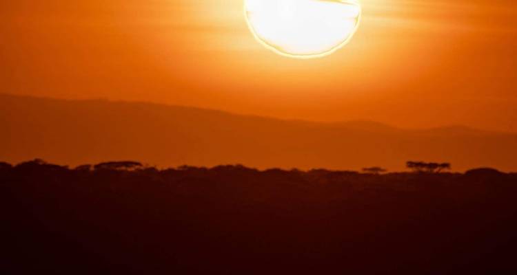 Sun setting over a silhouetted landscape.