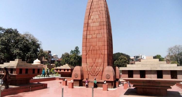 Denkmal mit Menschen in der Nähe, klarer Tag mit Bäumen rundherum.