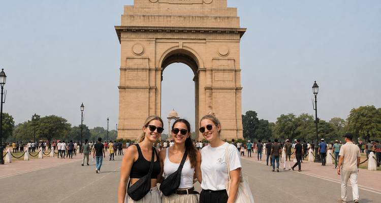 Trois jeunes femmes posant devant le monument de la Porte de l'Inde par une journée dégagée avec des foules en arrière-plan.