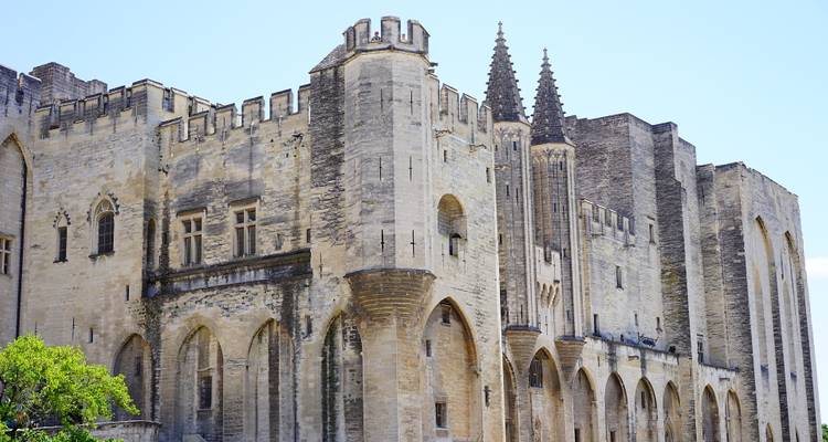 Remparts de pierre et tours pointues du Palais des Papes s'élevant contre un ciel dégagé à Avignon.