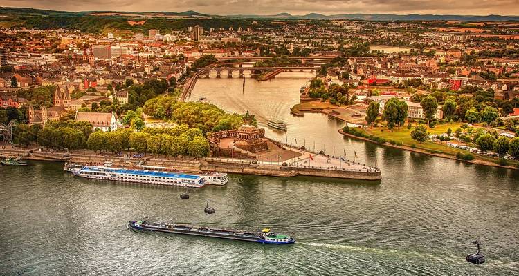 Luftaufnahme von Koblenz, wo Rhein und Mosel zusammenfließen, mit dem Deutschen Eck und vorbeifahrenden Flussschiffen.