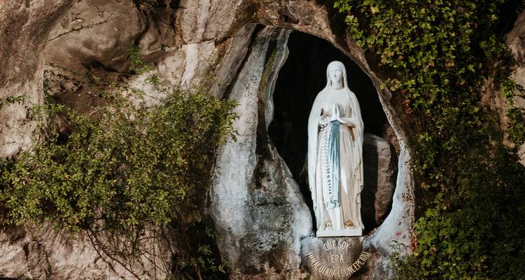 Statue illuminée de la Vierge Marie à l'intérieur d'une grotte rocheuse naturelle entourée de verdure