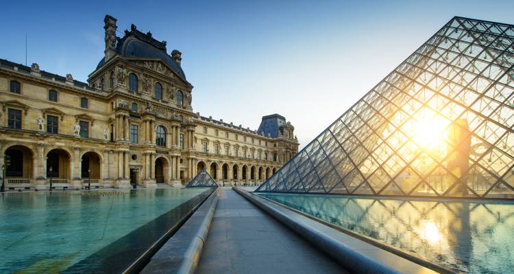 Les premiers rayons du soleil brillent à travers la Pyramide du Louvre, aux côtés de la façade classique du palais et des bassins de réflexion tranquilles.