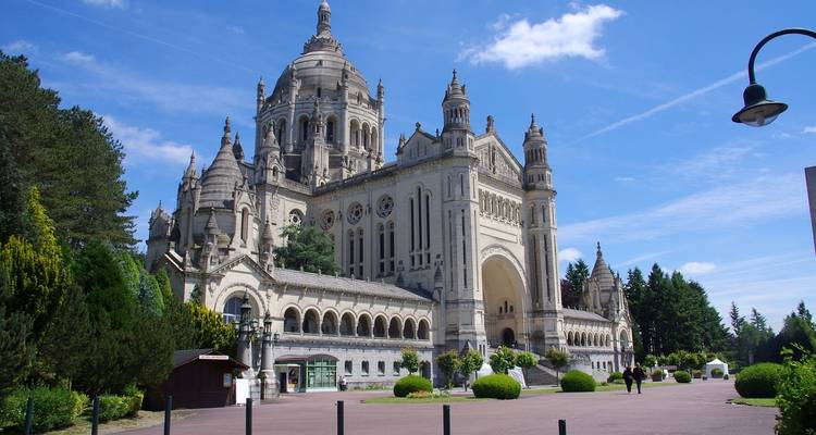 Grand basilica with ornate domes and towers framed by green gardens under a blue sky.