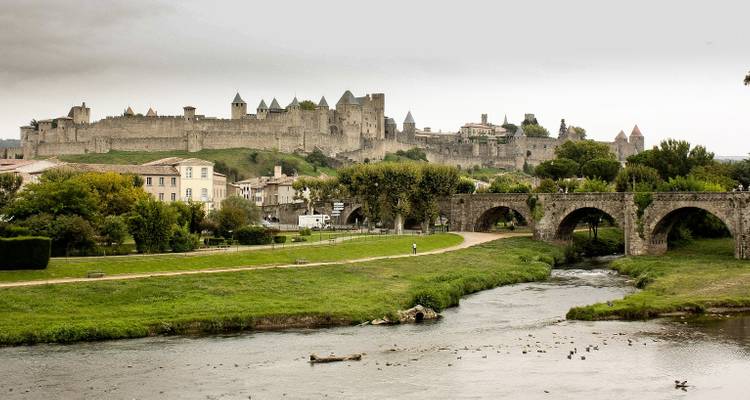 Medieval walled city of Carcassonne rises beyond an old stone bridge over a gentle river.