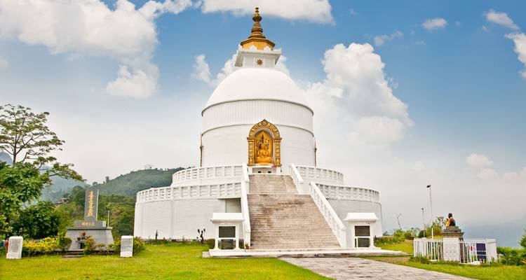 Weiße Stupa auf einem Hügel unter einem bewölkten Himmel.