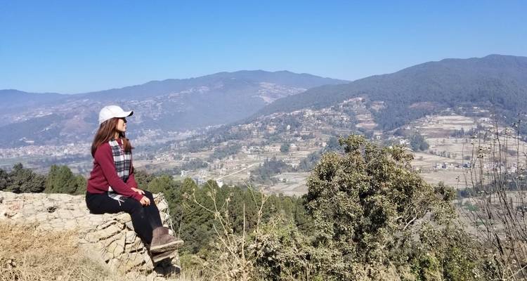 Mujer sentada en una roca, contemplando un vasto paisaje.