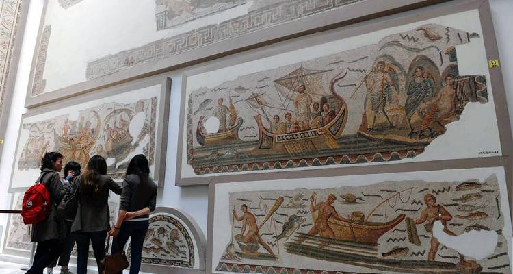 Interior de museo con mosaicos y un grupo de personas observando.