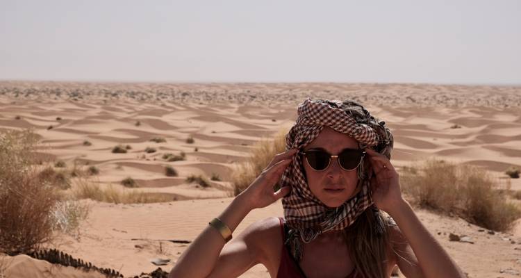 Woman in the desert wearing sunglasses and a headscarf.