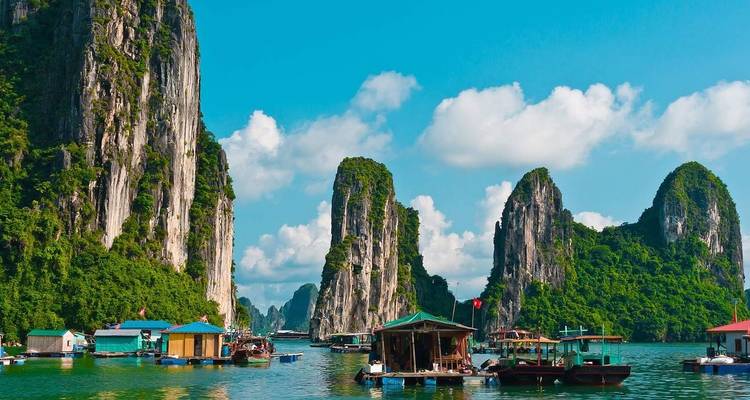 Floating villages and limestone karsts in a bay under a clear sky.
