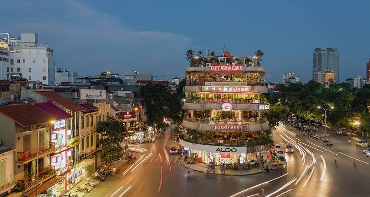 Lively city scene with a roundabout and a building with cafes and restaurants at night.