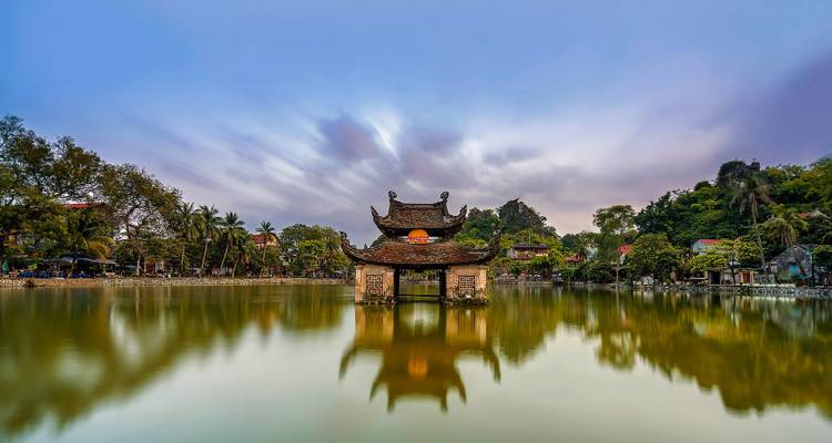 Pagoda vietnamita tradicional a orillas de un lago reflejada en agua tranquila con nubes que se mueven rápidamente y borrosas arriba.